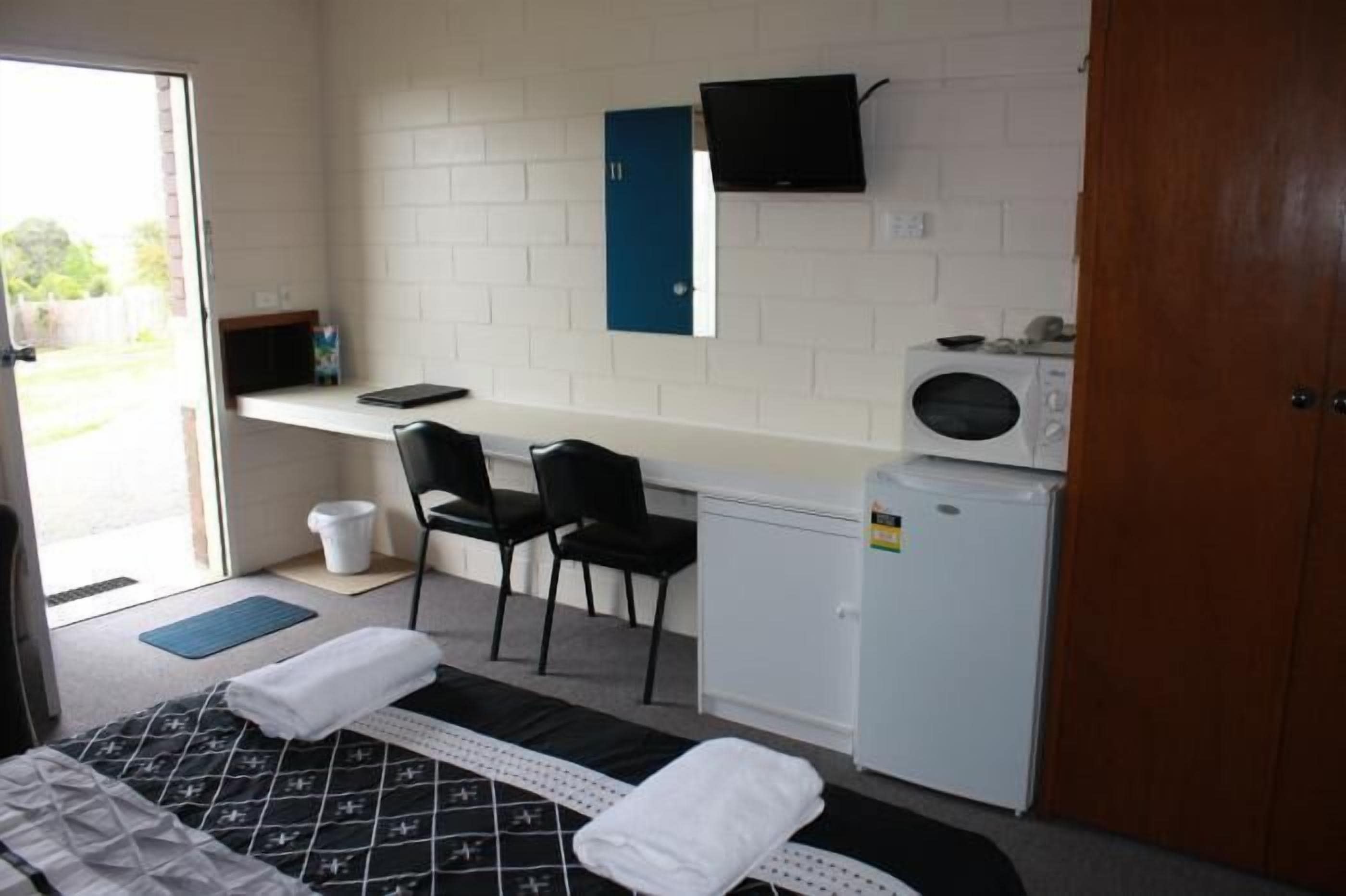 A compact hotel room with a bed, a desk with a computer, a microwave, and a small refrigerator.