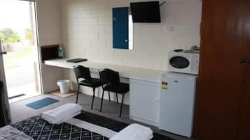 A compact hotel room with a bed, a desk with a computer, a microwave, and a small refrigerator.