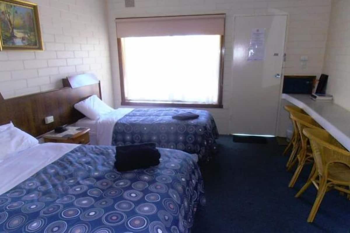 Una habitación con dos camas, una ventana, un escritorio con silla y un televisor.