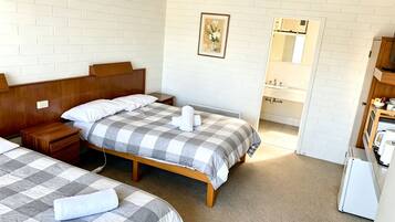 A hotel room with two beds, a wooden headboard, a bedside table, a nightstand, a ceiling fan, a bathroom with a sink and mirror, and a small kitchenette.