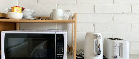 Una cocina equipada con microondas, tostadora y una estantería con vajilla y vasos.