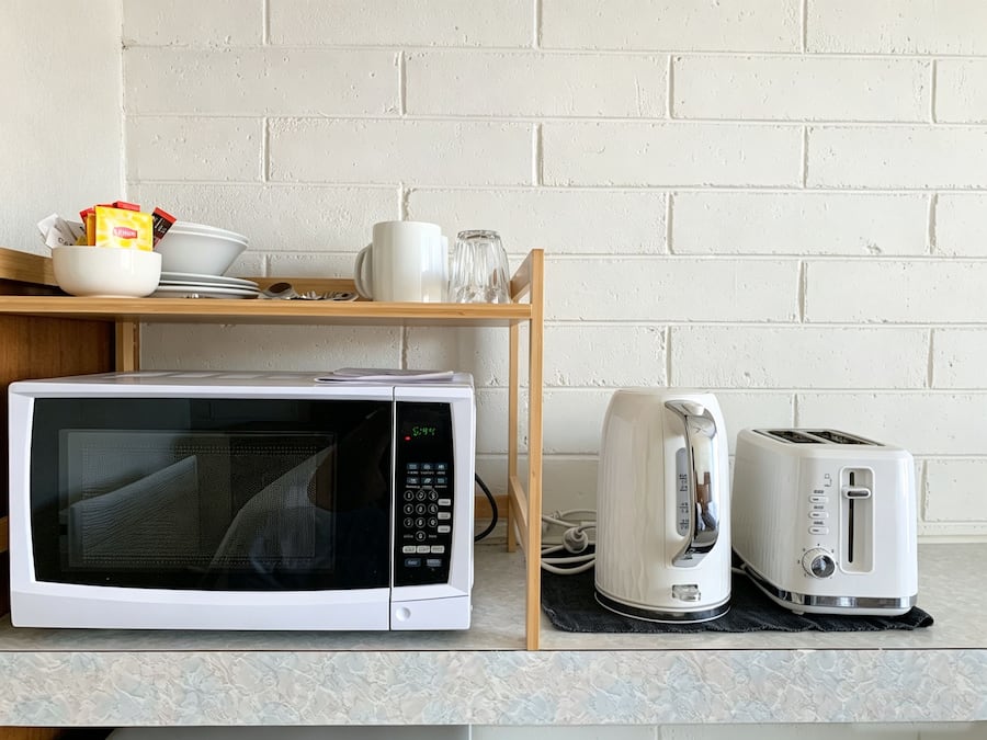 Una cocina equipada con microondas, tostadora y una estantería con vajilla y vasos.
