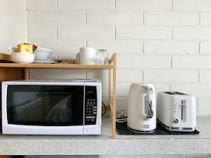 Una cocina equipada con microondas, tostadora y una estantería con vajilla y vasos.