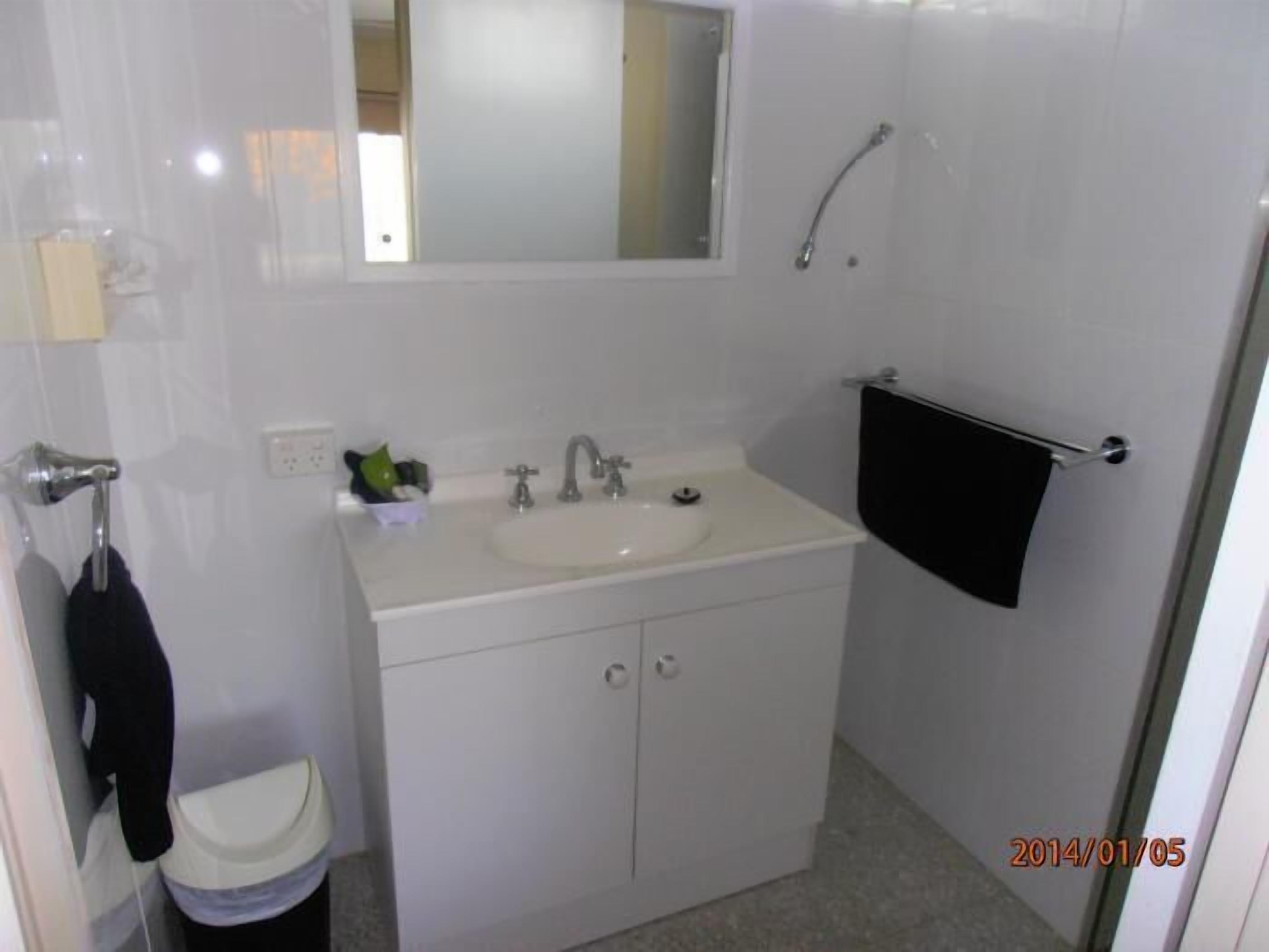 Een kleine, schone badkamer met een wit wastafelmeubel, spiegel en handdoekhouder.