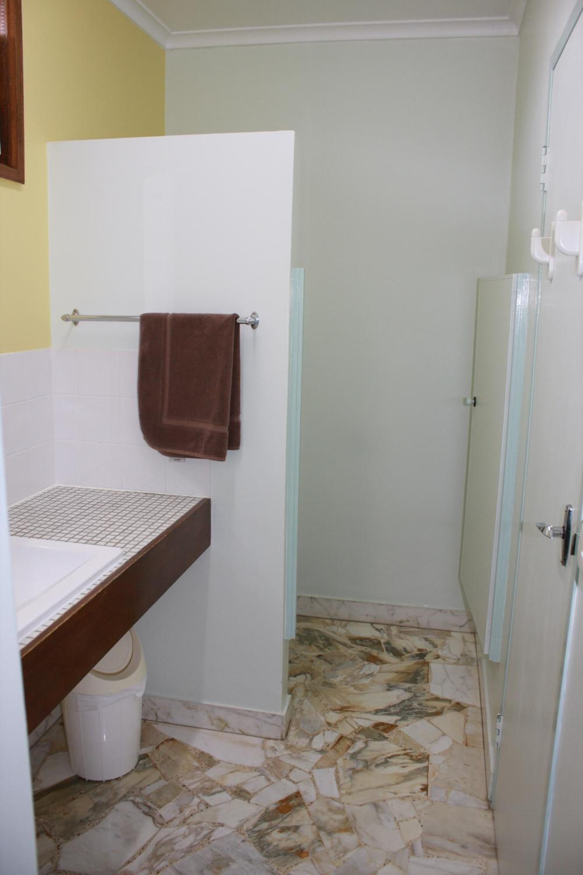 Un baño con un lavamanos blanco, una toalla marrón colgada en un perchero, piso con estampado de mármol y cabina de ducha de vidrio.