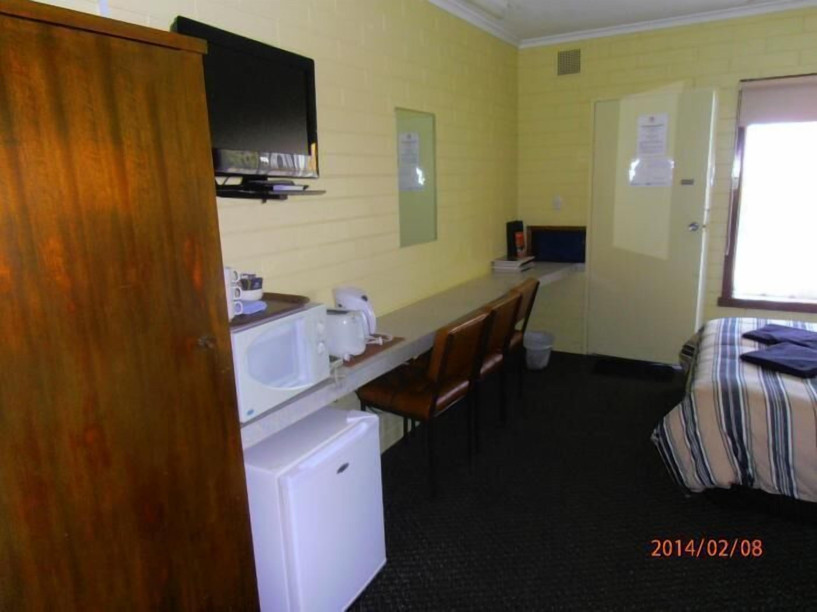 A compact hotel room with a kitchenette, a bed, and a single chair.
