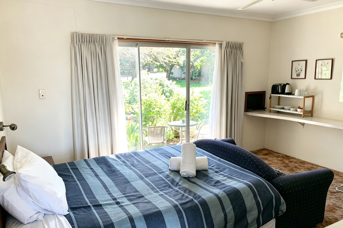 Habitación de hotel con una cama, una ventana con cortinas, una mesita y un estante con objetos.