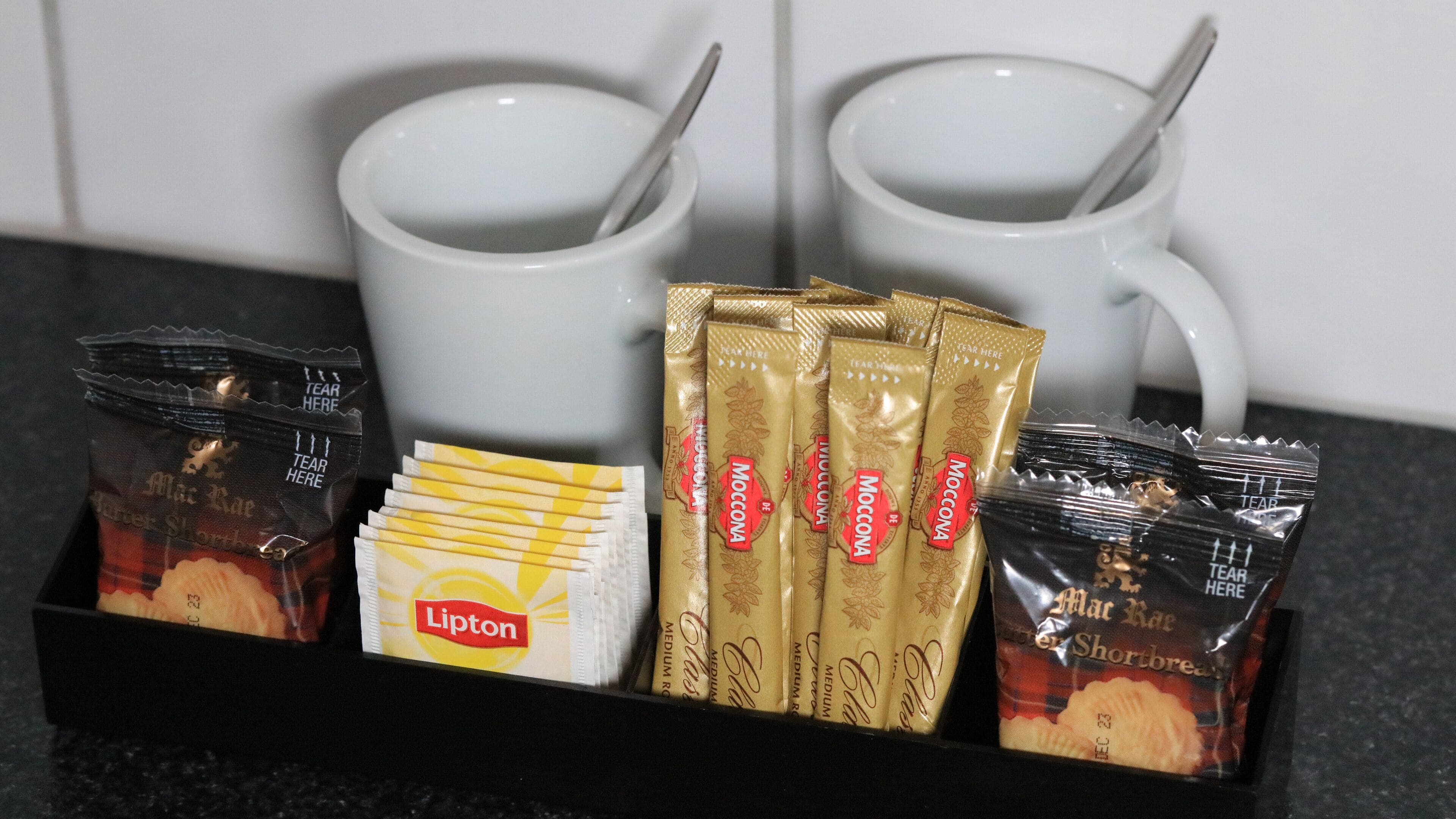 A tray with coffee packets, Lipton tea, and two white mugs with spoons.