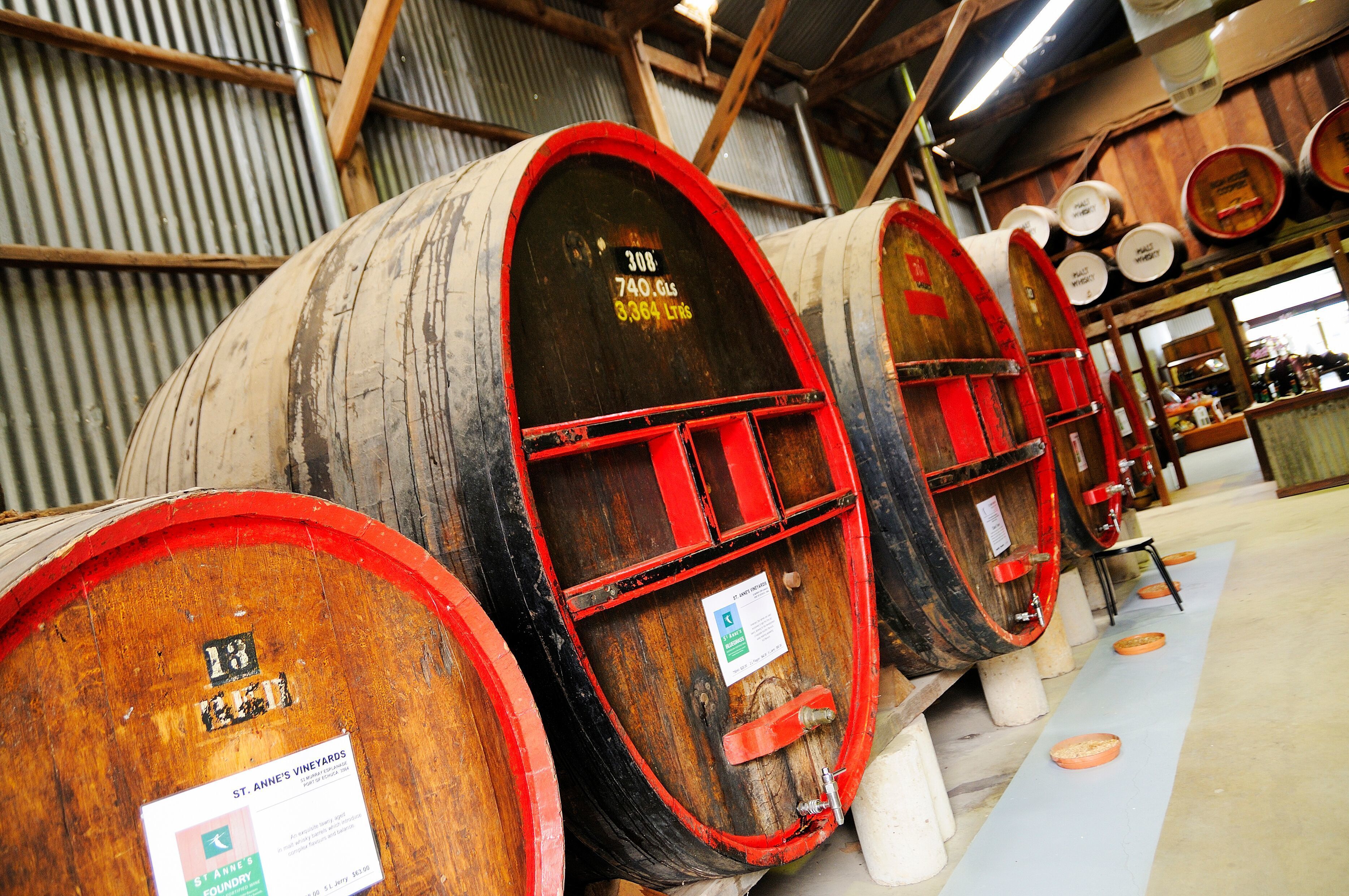 Large wooden barrels with red interiors, arranged in a row inside a warehouse with metal walls and wooden beams.