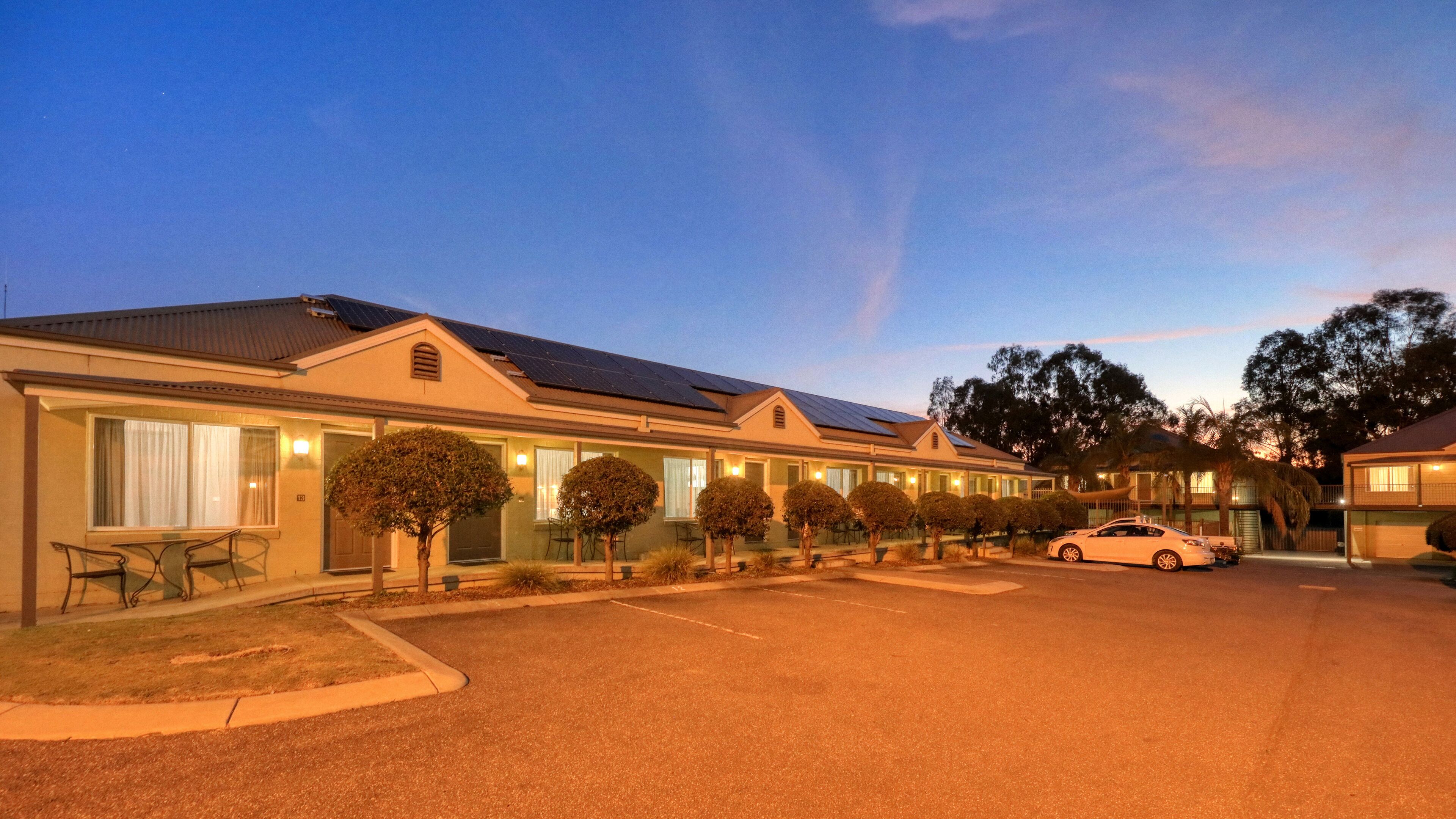 A row of motel buildings with solar panels, a covered parking area, and a car parked in front.