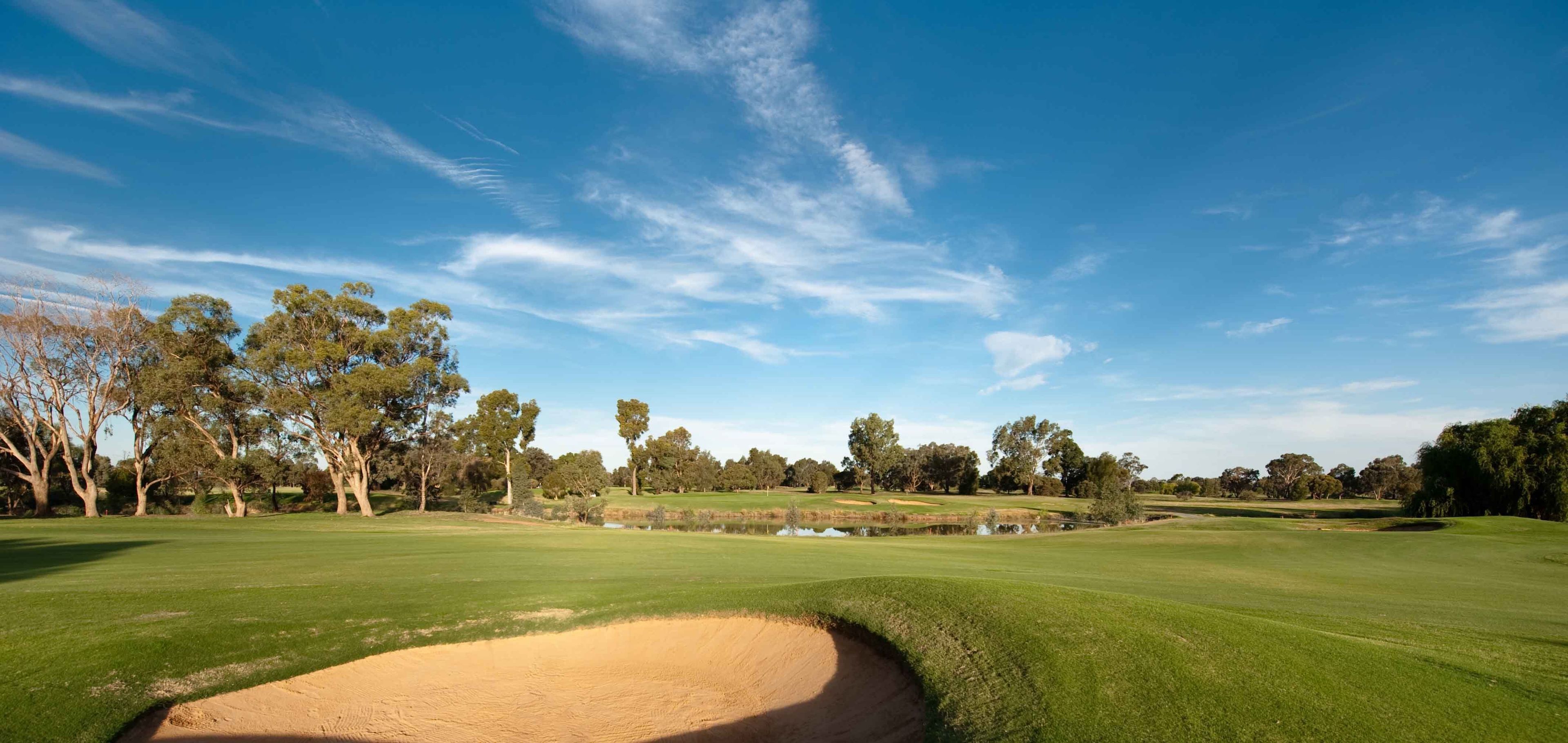 Un campo de golf con búnkeres de arena, obstáculos acuáticos y árboles.