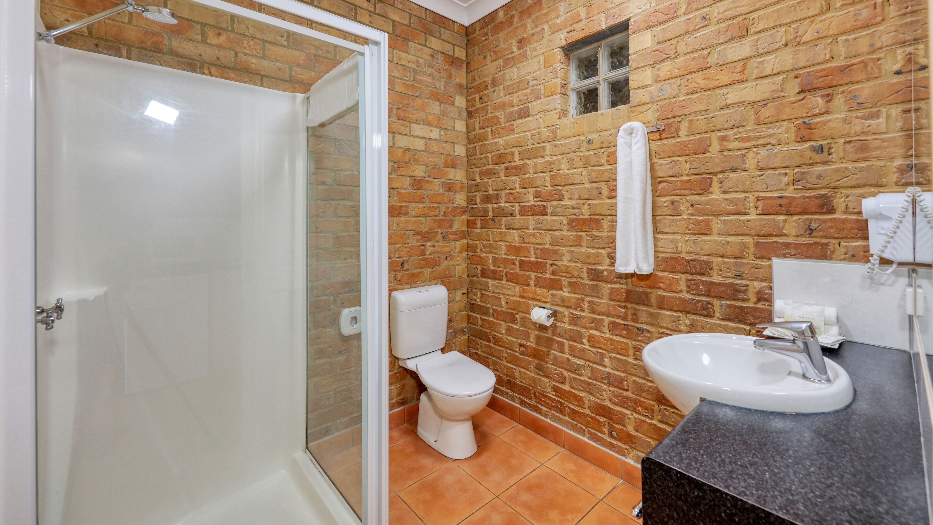 A bathroom with a glass shower enclosure, a toilet, a sink, and a towel hanging on the wall.