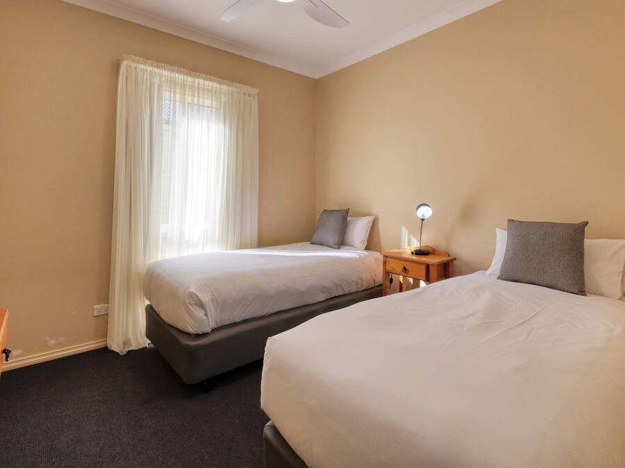 A hotel room with two beds, a desk, a nightstand with a lamp, and a window with curtains.