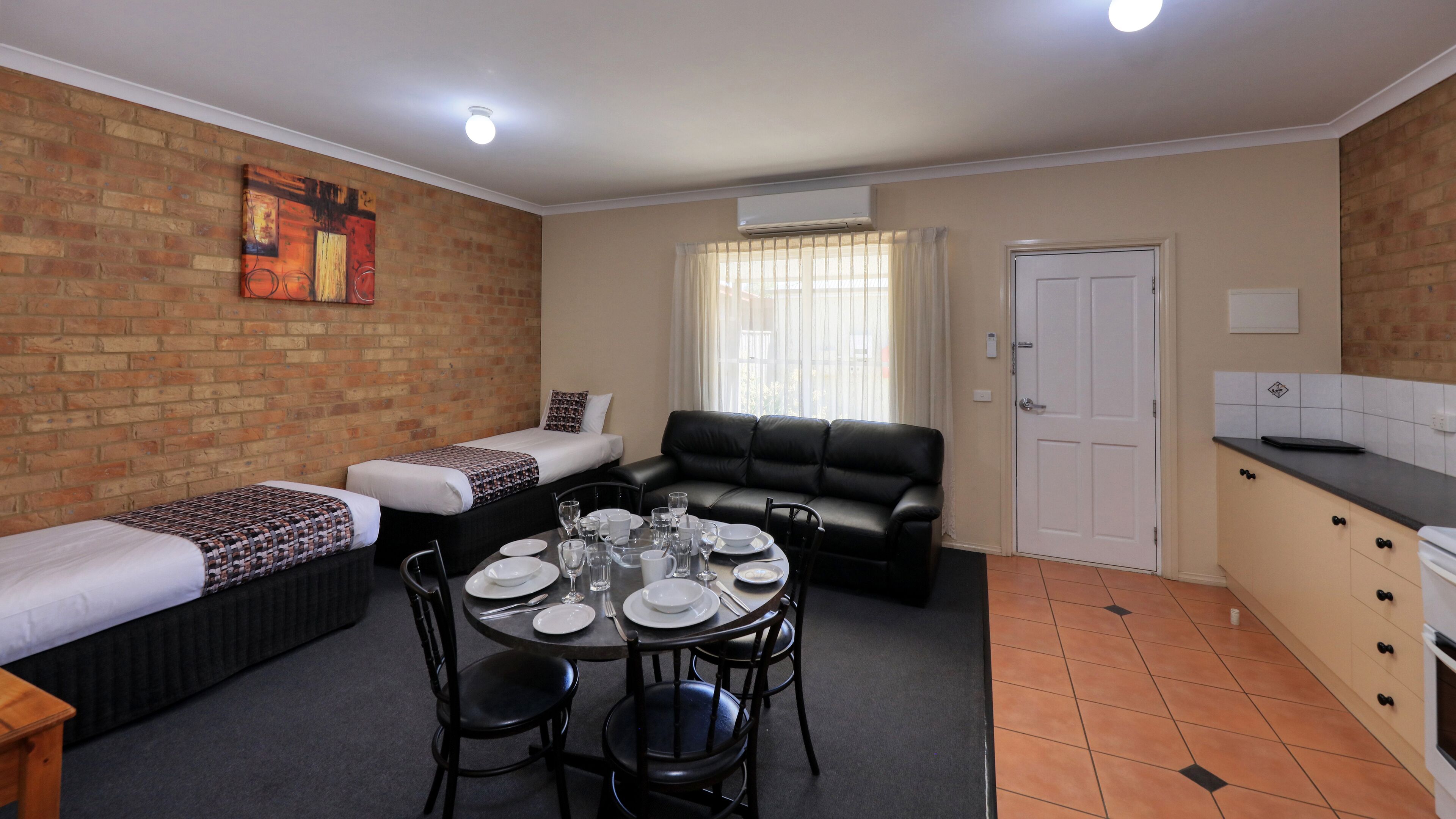 A compact living space with a dining area, a sofa, a small kitchen, and a brick wall.