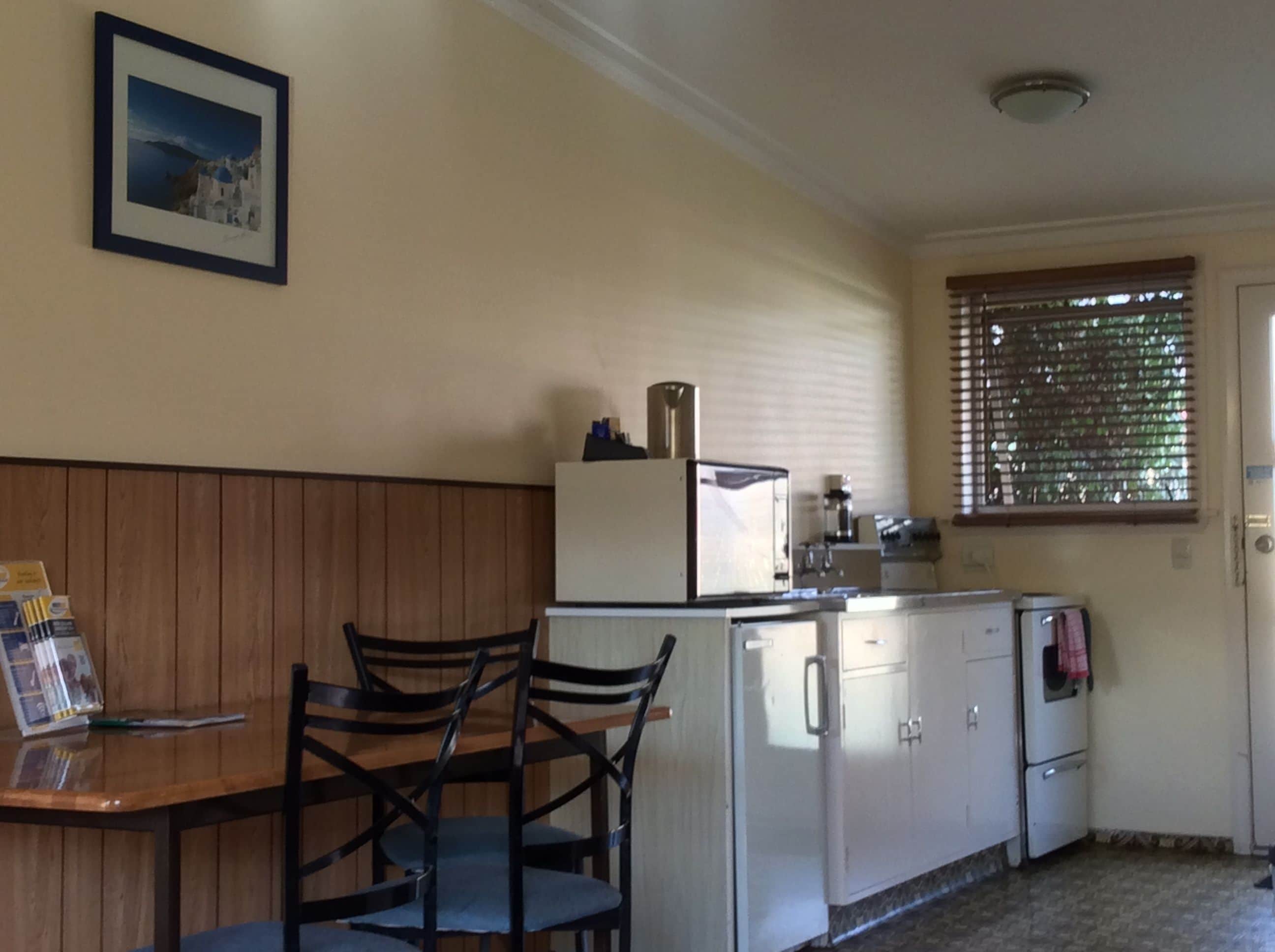 Cocina compacta con refrigerador, estufa y lavaplatos. Hay una mesa de madera con sillas y un cuadro en la pared.