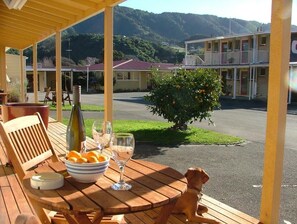 A wooden deck with a table set for two, a bowl of oranges, and a bottle of wine. A dog is sitting on the deck. - AAA Marlin Motel (Picton)