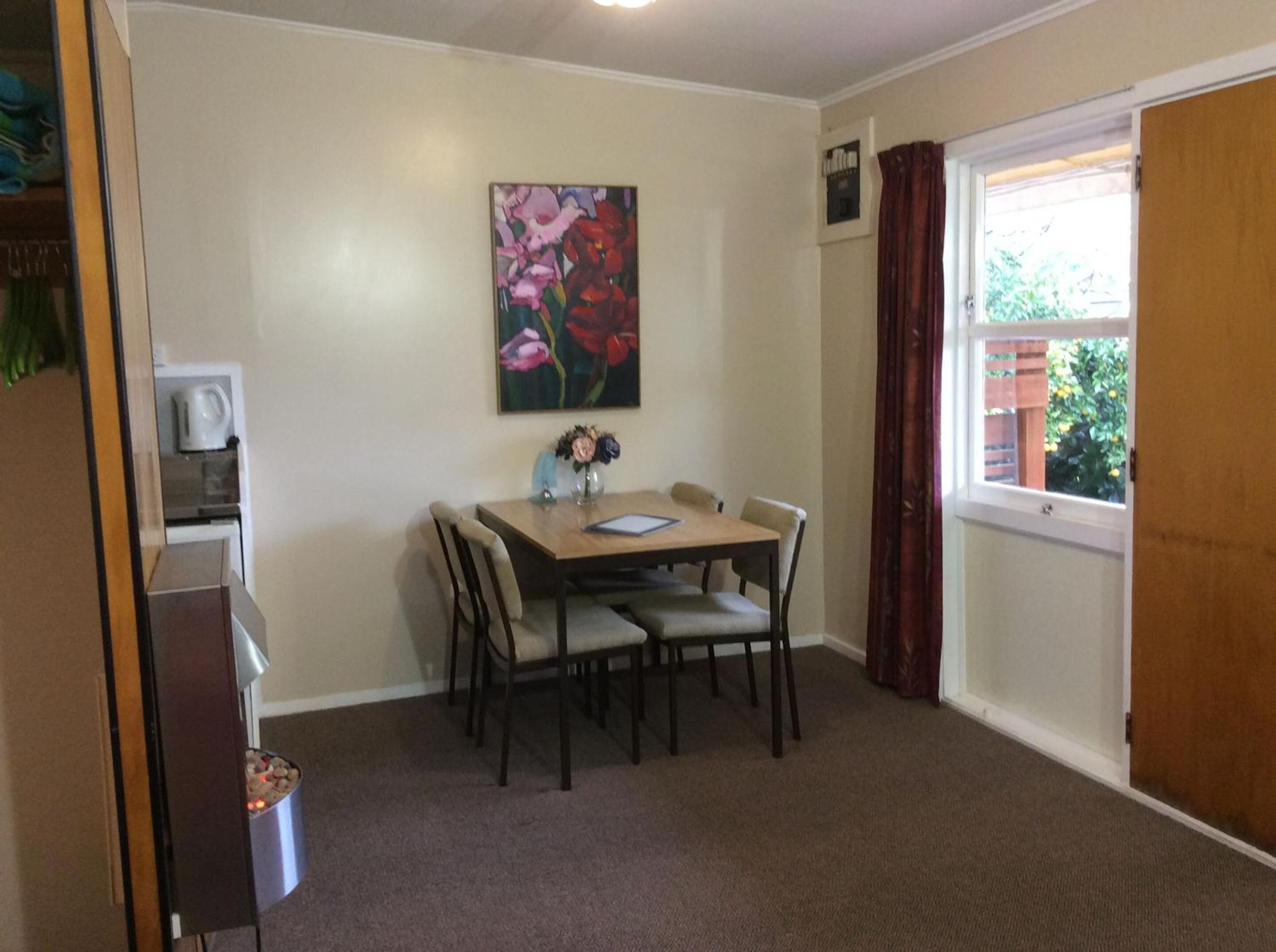 Un comedor con una mesa preparada para cuatro personas, un cuadro en la pared y una ventana con cortinas.