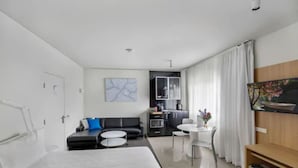 A modern hotel room with a large bed, a sofa, a dining table, and a TV. - The Horatio - Suites & Motel (Mudgee)