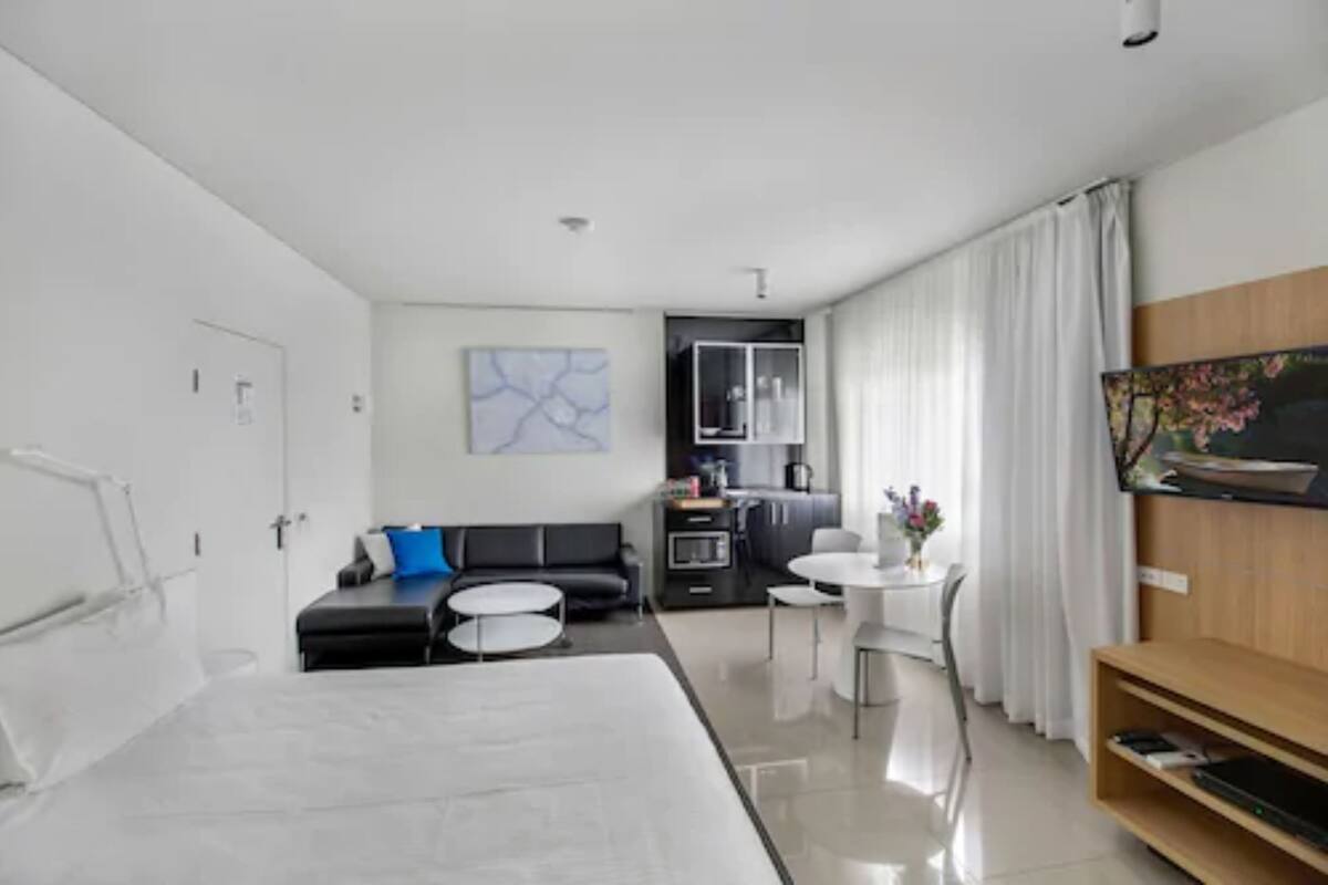 Ein modernes Hotelzimmer mit einem großen Bett, einer Couch, einem Esstisch und einem Fernseher.
