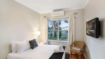 A hotel room with a bed, a chair, a window, and a wall-mounted TV.