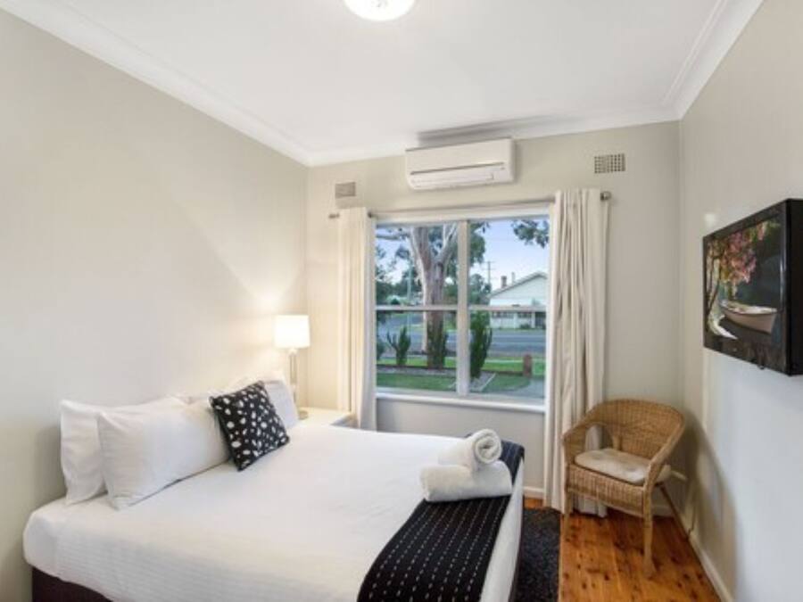 A hotel room with a bed, a chair, a window, and a wall-mounted TV.