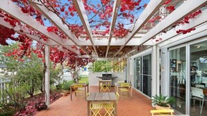 An outdoor patio area with tables and chairs, a grill, and a pergola covered with red leaves. - The Horatio - Suites & Motel (Mudgee)