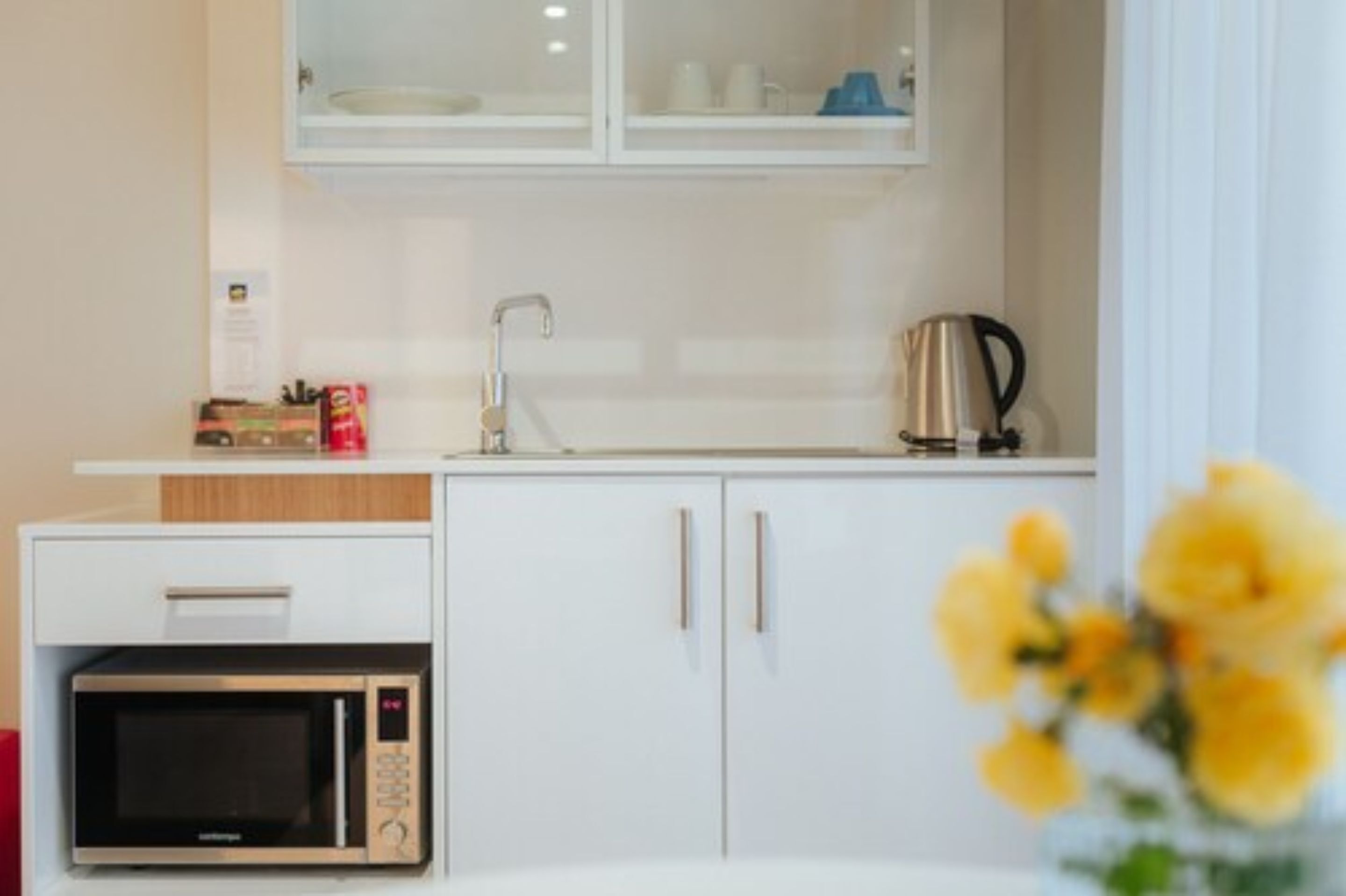 Una kitchenette compacta con microondas, cafetera y un mueble con lavabo.