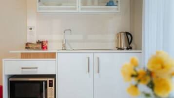Una kitchenette compacta con microondas, cafetera y un mueble con lavabo.