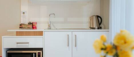 Una kitchenette compacta con microondas, cafetera y un mueble con lavabo.