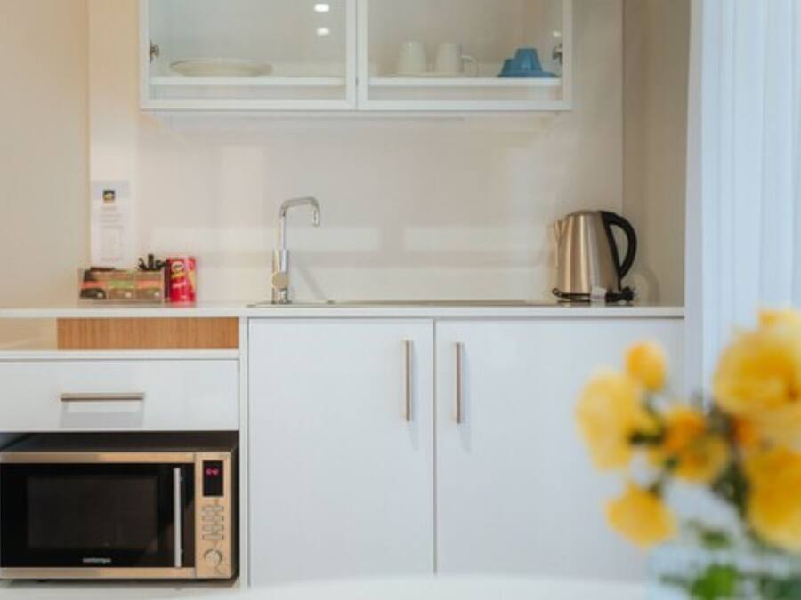Una kitchenette compacta con microondas, cafetera y un mueble con lavabo.