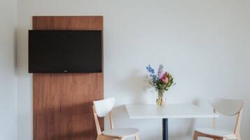 Een moderne kamer met een witte tafel, twee houten stoelen, een houten paneel en een flatscreen televisie aan de muur.