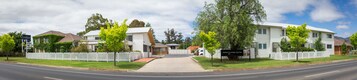 Un motel con zona de recepción, aparcamiento y una cerca blanca de piquetes alrededor de la propiedad.