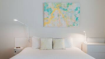 A bedroom with a large bed, two bedside tables, a wall-mounted abstract painting, and a white nightstand.