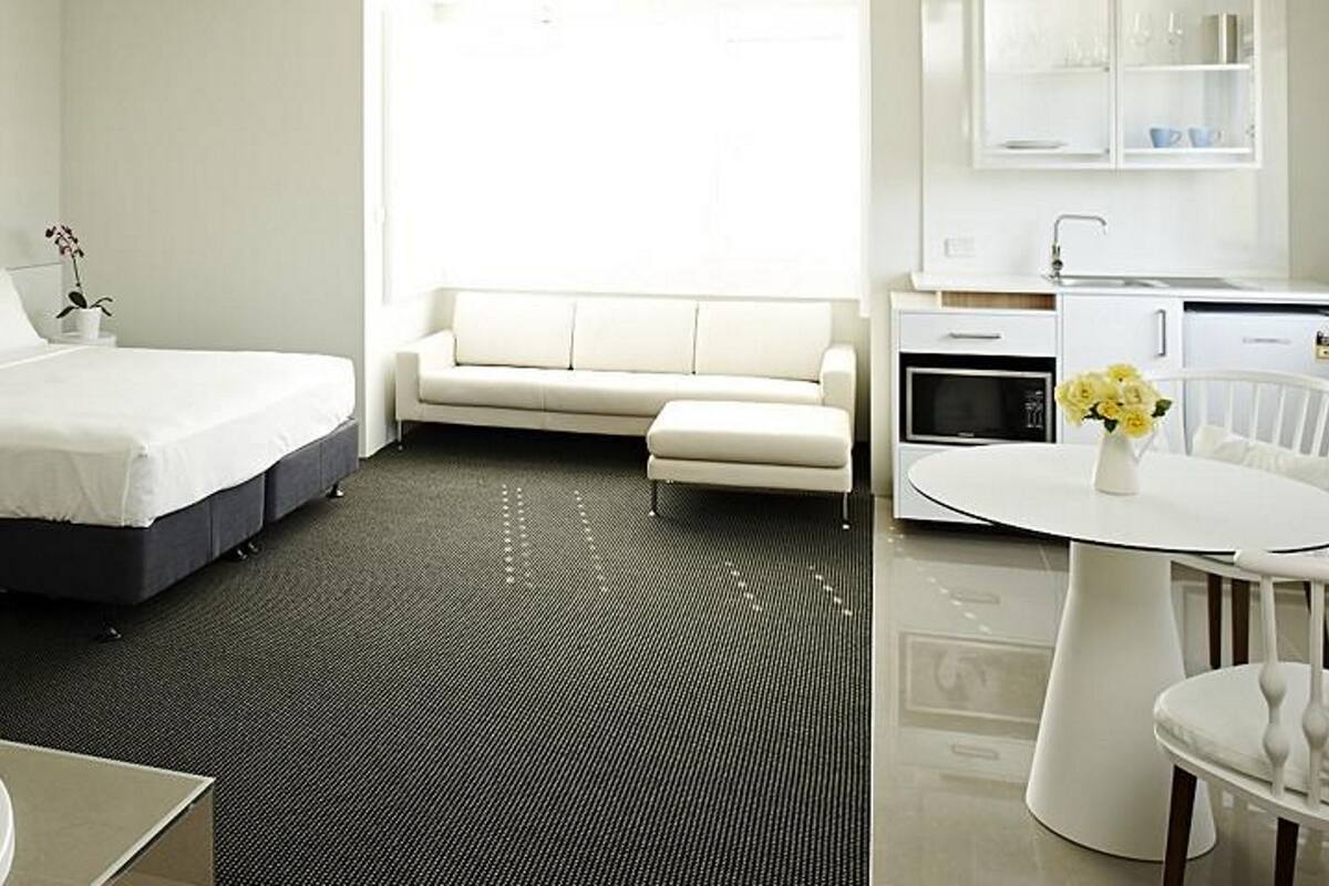 Ein modernes Hotelzimmer mit einem großen Bett, einer Sitzecke, einem kleinen Tisch, einem Badezimmer mit Badewanne und einer Küchenzeile.