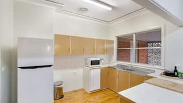 Cocina compacta con armarios blancos, un microondas y una ventana con vista a un muro de ladrillo.