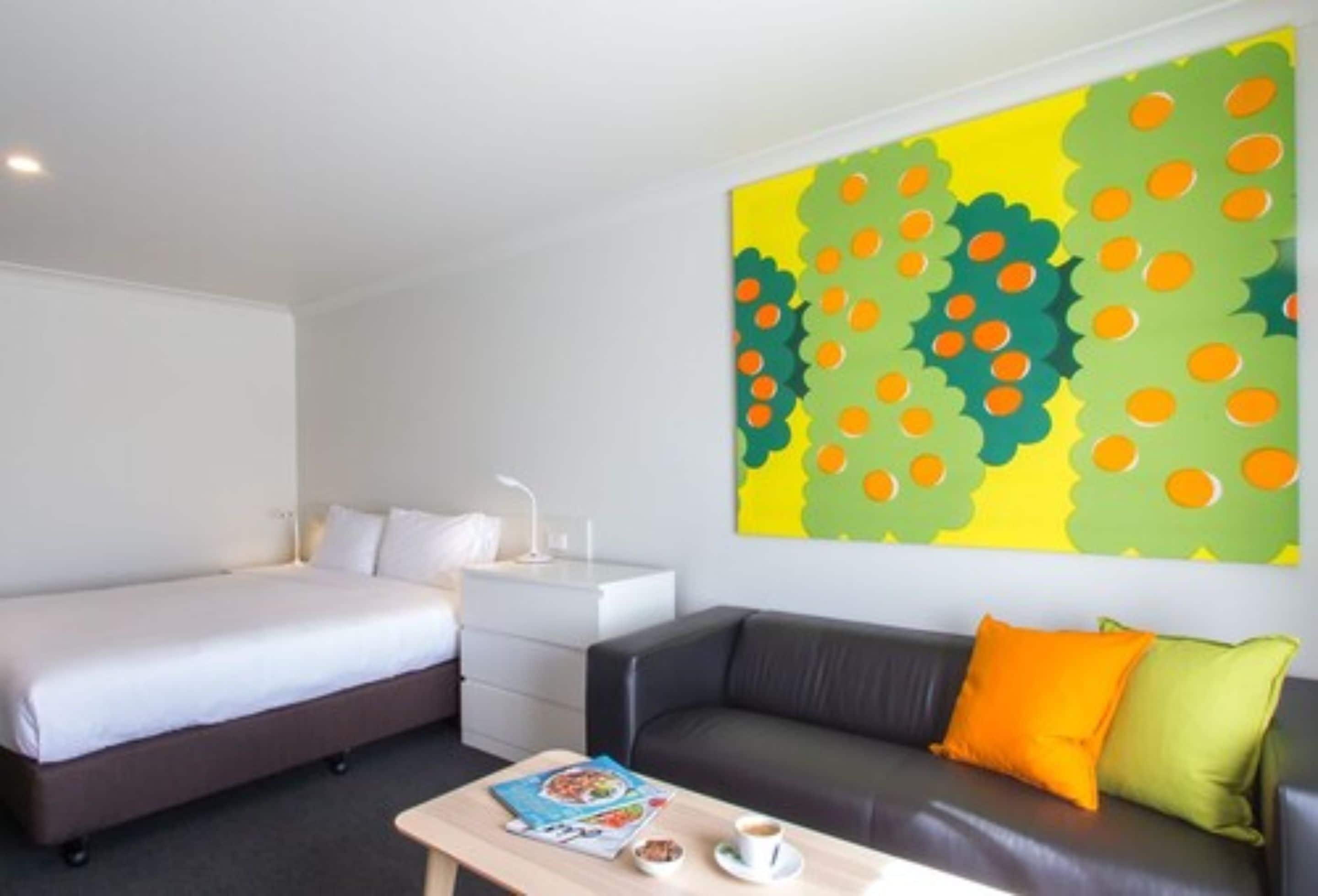 A hotel room with a bed, a sofa, a coffee table, and a large abstract painting on the wall.