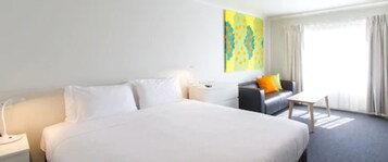 Habitación de hotel con una cama grande, un sofá, una mesita y un cuadro en la pared.
