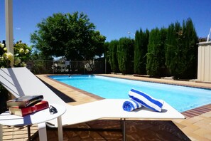 Une piscine avec un fauteuil de relaxation blanc, une serviette et des livres sur une petite table.