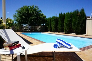Una piscina con una silla de descanso blanca, una toalla y libros sobre una mesita.