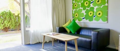 A room with a black leather sofa, a wooden coffee table, and a large floral wall art piece.