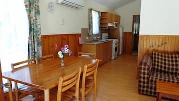 A dining area with a wooden table and chairs, a small kitchen area with a stove and refrigerator, and a living area with a sofa and a patterned cushion.