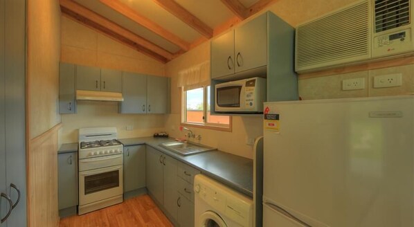 A compact kitchen with a gas stove, oven, microwave, sink, and a washing machine.
