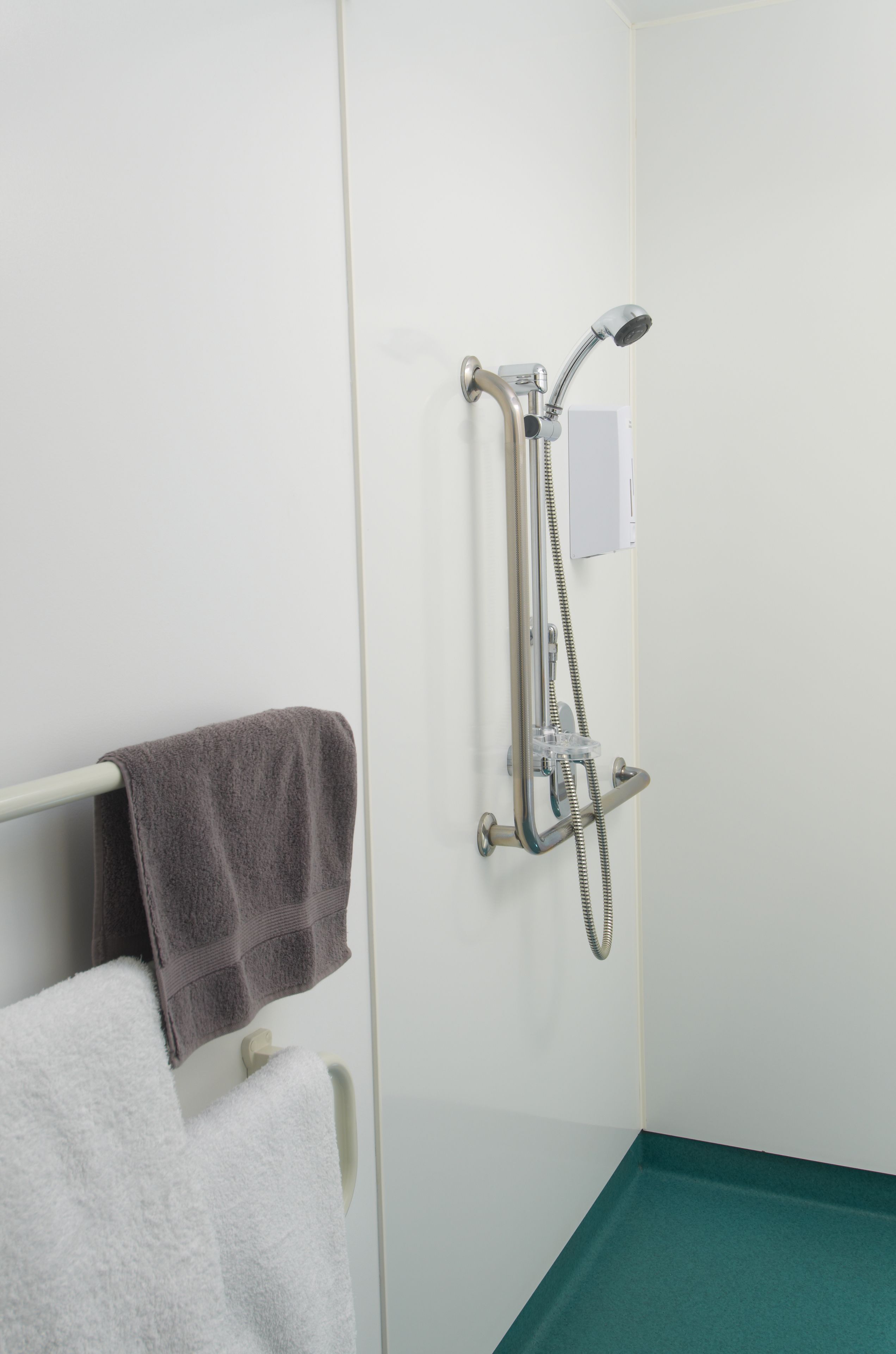Un baño con ducha, toallero y suelo verde.