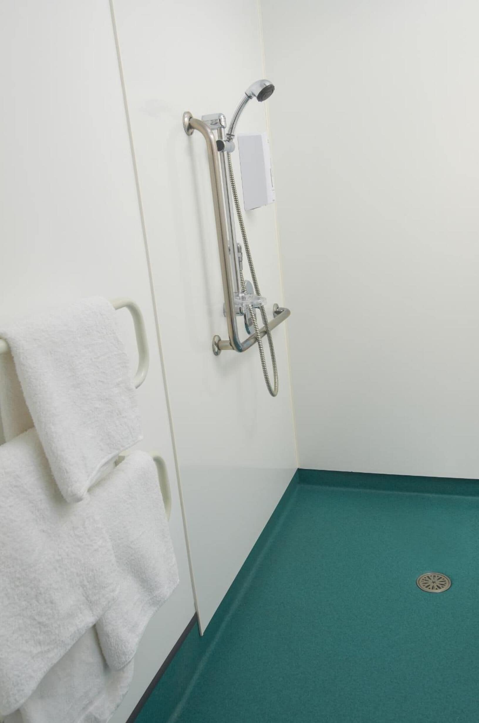 Une salle de bain avec une douche, des serviettes blanches et un sol vert.