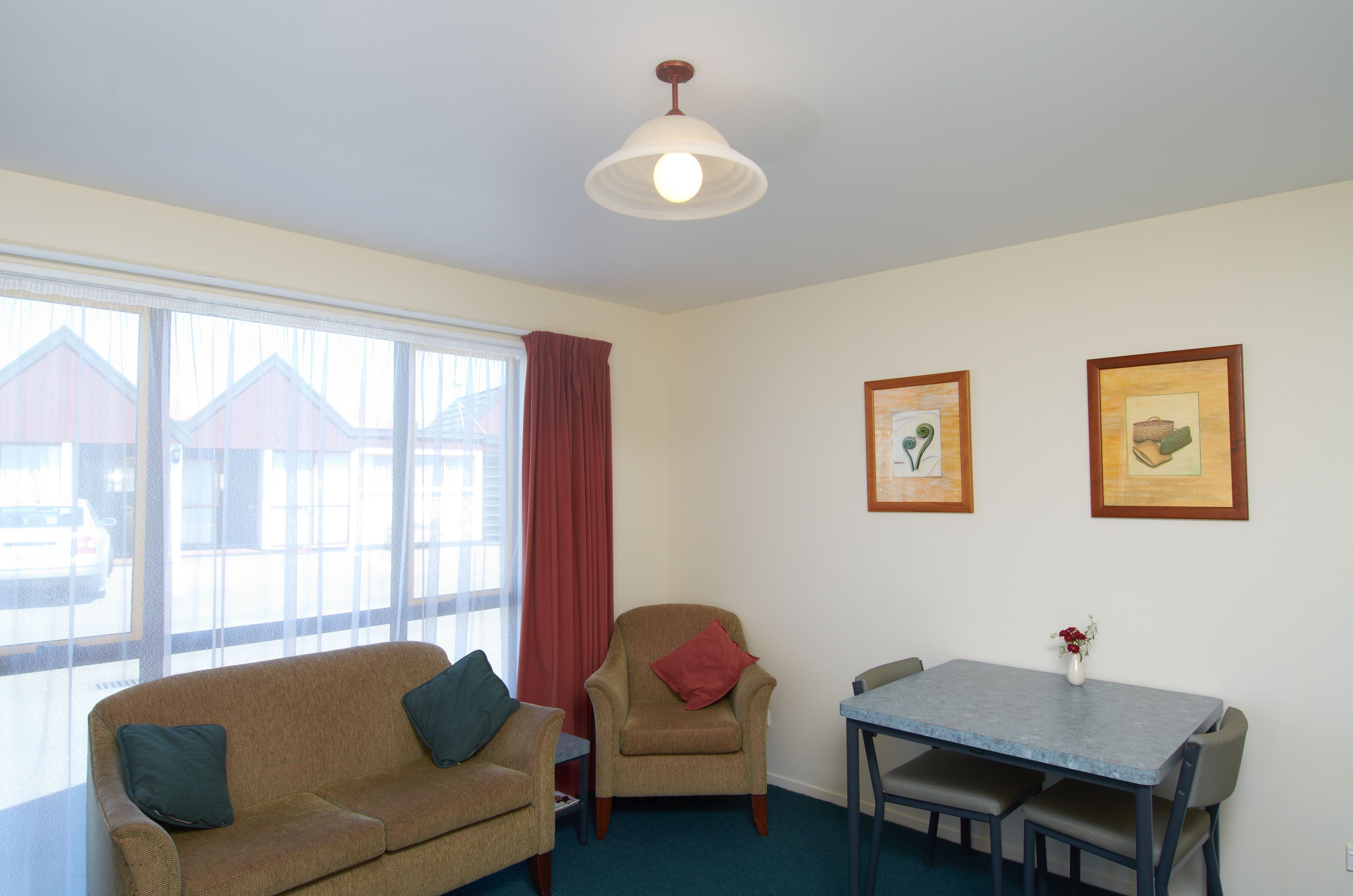 A room with a sofa, armchair, dining table, and two framed pictures on the wall.