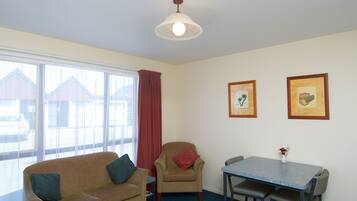 A room with a sofa, armchair, dining table, and two framed pictures on the wall.