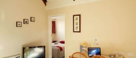 Habitación de hotel con televisión, una laptop sobre un escritorio, una silla de madera y una cama con una manta roja.