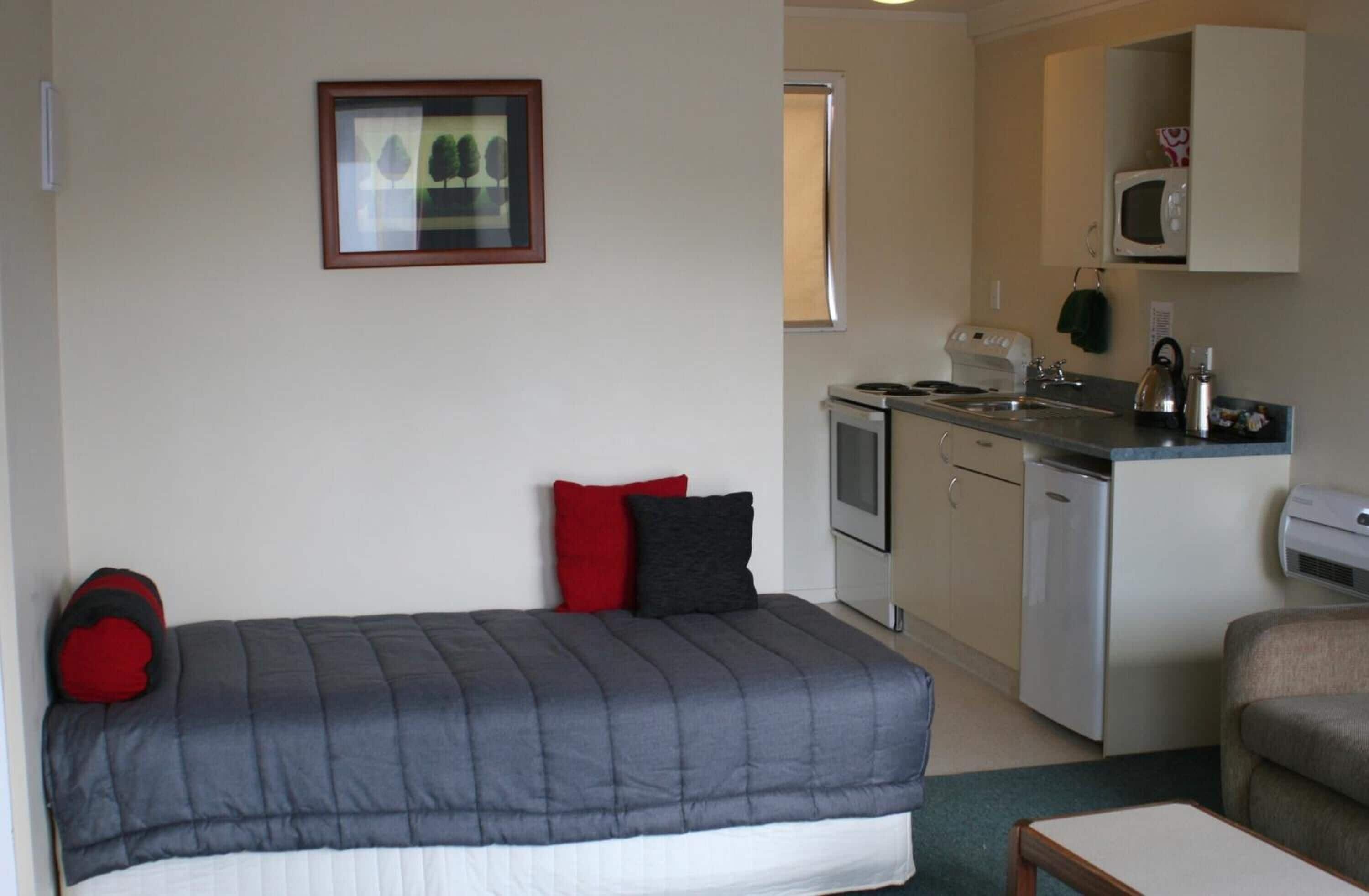 A compact room with a bed, a small kitchenette, and a single chair.