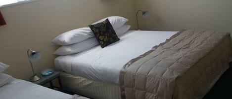 Habitación de hotel con dos camas, una mesita de noche con lámpara y una ventana con cortinas.