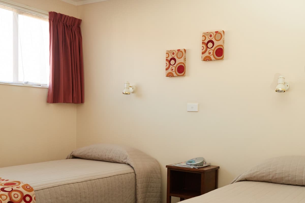 Quarto de hotel com duas camas, uma janela com cortinas e obras de arte nas paredes.